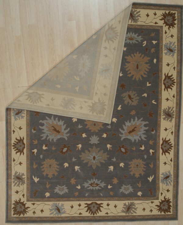 Dark gray floral rug featuring cream, tan, and blue accents, partially folded on light wood planks.