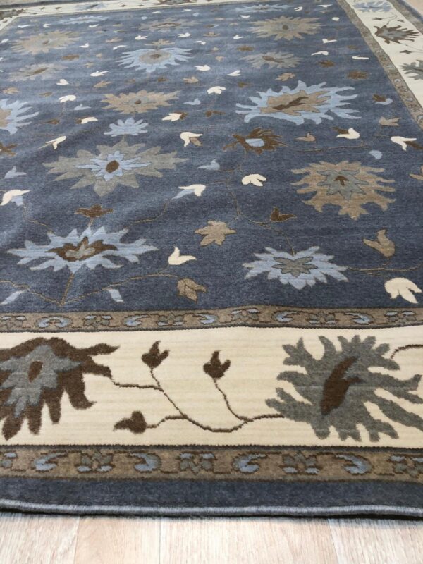Dark blue high-pile rug featuring light blue and taupe stylized flowers, with a wide cream border on wood plank flooring.