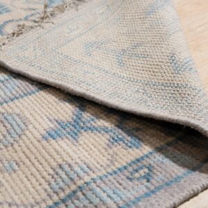 Blue and gray geometric patterned rug with medium pile curled back on light wood flooring.