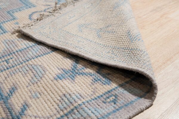 Blue and gray geometric patterned rug with medium pile curled back on light wood flooring.