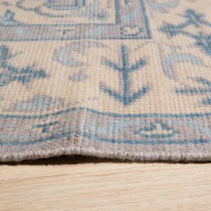 Close-up of a cream rug with blue and gray geometric patterns resting on light wood floors.