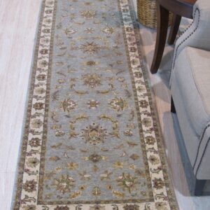 Long blue-gray runner rug with floral pattern next to a beige armchair and round dark wood table.
