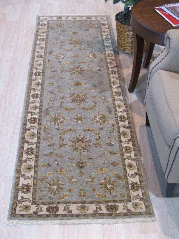 Long blue-gray runner rug with floral pattern next to a beige armchair and round dark wood table.
