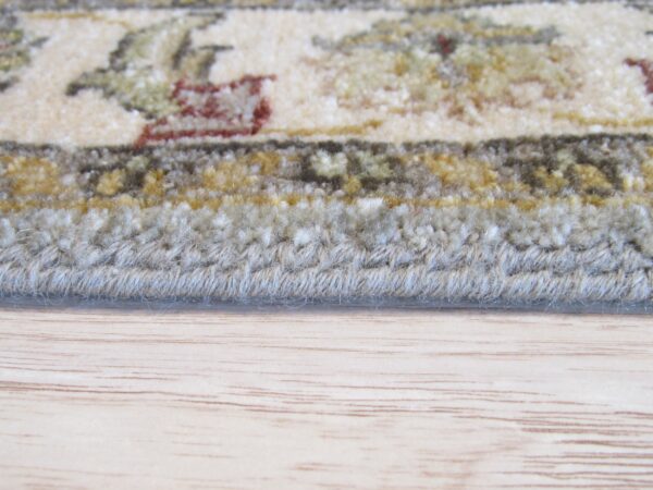 Close-up of a floral rug edge showing cream, green, and rust patterns, resting on light wood flooring.