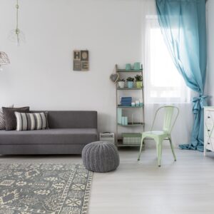The gray medallion rug complements a gray couch, knitted pouf, and mint chair on light flooring.
