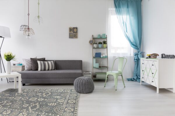 The gray medallion rug complements a gray couch, knitted pouf, and mint chair on light flooring.