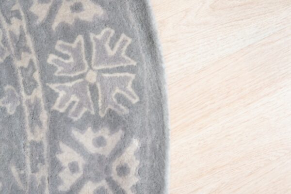 Close-up of a plush gray rug with an abstract beige geometric pattern on light wood flooring.