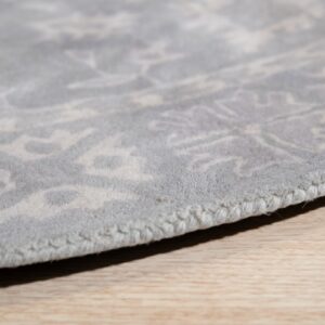 Detailed close-up of a low-pile light grey rug edge showing a tonal pattern on light wood flooring.
