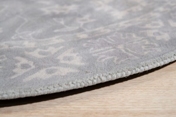 Detailed close-up of a low-pile light grey rug edge showing a tonal pattern on light wood flooring.