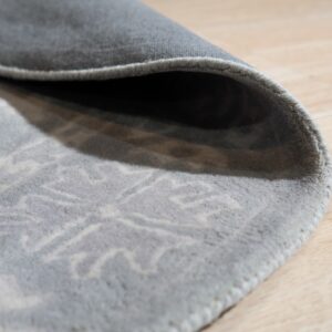 The curled edge of a low-pile gray rug with a light patterned design rests on blonde wood flooring.