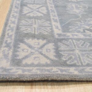 Angled view of a plush gray rug with white traditional border design resting on light wood plank flooring.