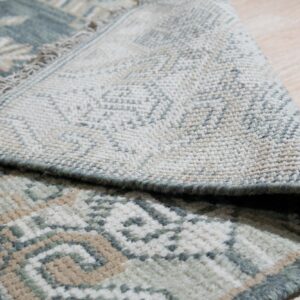 Detail view of a low-pile rug in sage, tan, and cream, showing the fringe and woven reverse side.