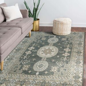 A sage green, beige, and cream traditional rug on dark wood floors beside a gray couch and woven ottoman.
