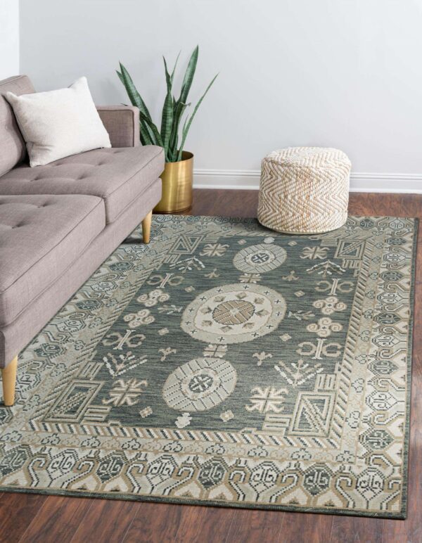 A sage green, beige, and cream traditional rug on dark wood floors beside a gray couch and woven ottoman.