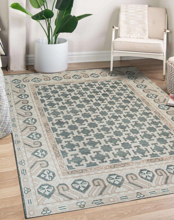 Teal and cream ornate geometric rug on wood floors beside a large plant and white armchair.