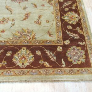 Intricate sage green and rust floral rug displayed on light blonde wood plank flooring.