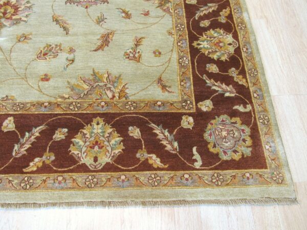 Intricate sage green and rust floral rug displayed on light blonde wood plank flooring.