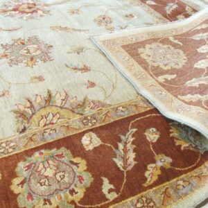 Traditional floral rug in pale green and rust, curled back to show the backing on a light wood floor.