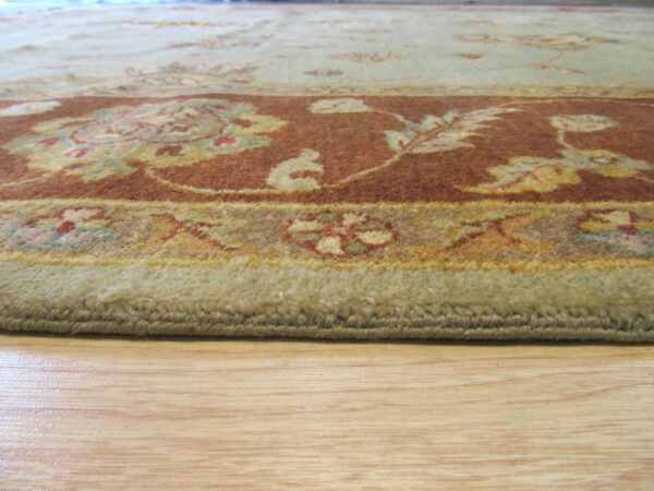 A medium-pile rug in sage and rust floral patterns rests on a light hardwood floor.