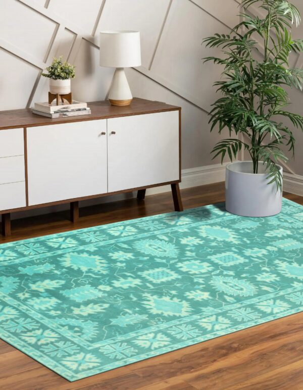 Teal patterned rug on wood flooring below a white and wood console table and large houseplant.