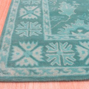 Textured teal and aqua rug displaying traditional borders and scrolling floral patterns on pinkish wood planks.