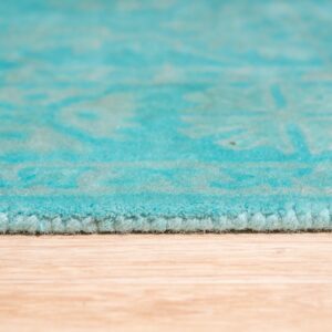 Close-up showing the plush turquoise rug edge and faint pattern on light wood floor.