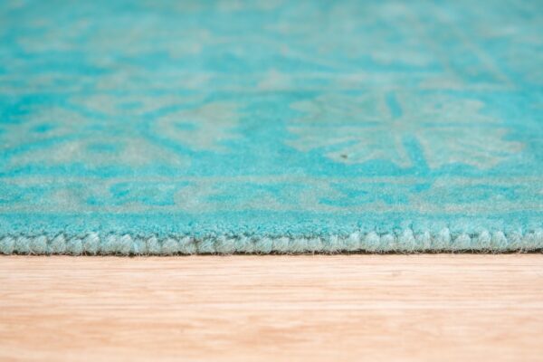 Close-up showing the plush turquoise rug edge and faint pattern on light wood floor.