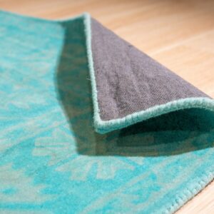 Turquoise low-pile rug with a pale pattern is rolled, showing the gray backing on light wood.