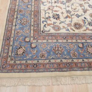Ornate cream rug with blue and rose floral borders resting on light wood flooring.