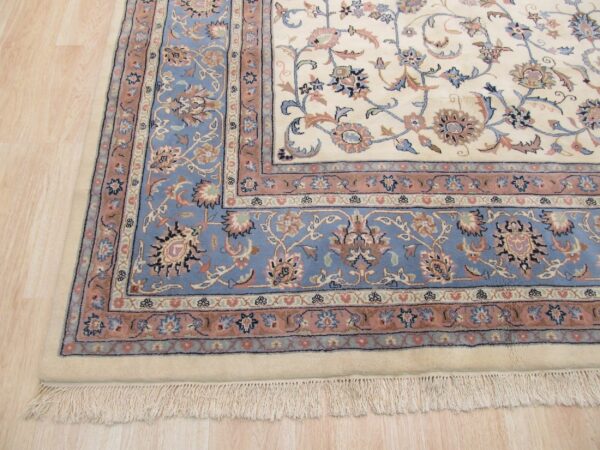 Ornate cream rug with blue and rose floral borders resting on light wood flooring.
