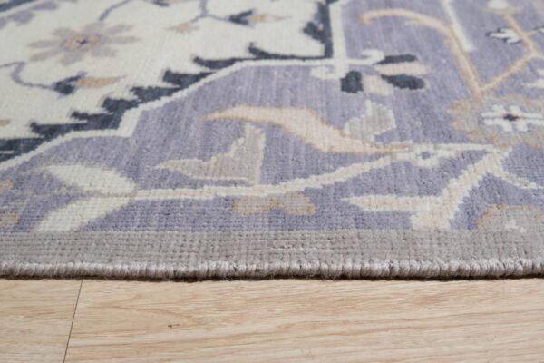 Traditional rug border featuring lavender, cream, and gray designs rests on light wood floors.