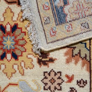 Close-up of a folded rug showing plush traditional patterns in gold, navy, and red contrasted with the tight woven backing.
