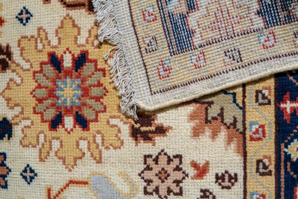 Close-up of a folded rug showing plush traditional patterns in gold, navy, and red contrasted with the tight woven backing.
