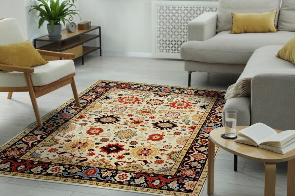 Cream and multicolored patterned rug placed on light wood floor between a sofa and armchair.