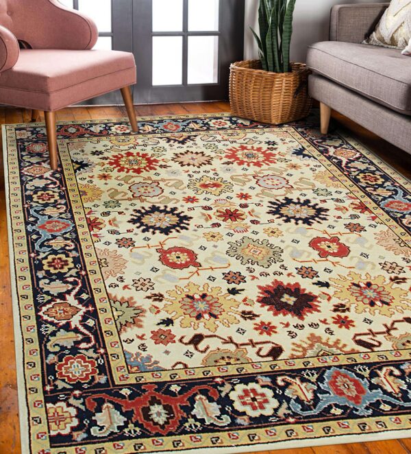 A cream rug featuring traditional multicolored floral medallions and a navy border sits on a wooden floor.