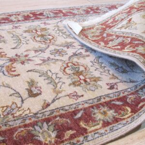 The corner of a light-colored rug with a red floral border is curled back on light wood flooring.