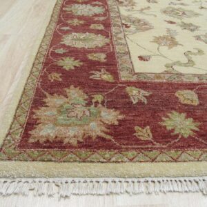 Traditional high-pile rug detail showing a cream field and red border with floral motifs on light wood flooring.