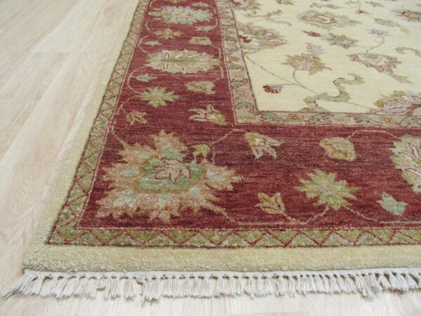 Traditional high-pile rug detail showing a cream field and red border with floral motifs on light wood flooring.