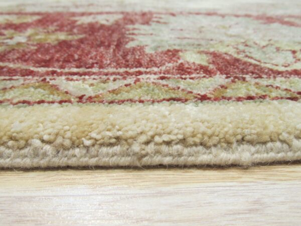 High-pile rug edge in cream, red, and sage patterns rests directly on light wood flooring.
