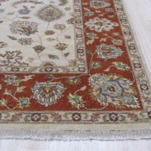Low-pile rug with a cream field and rust floral border resting on pale wood flooring.