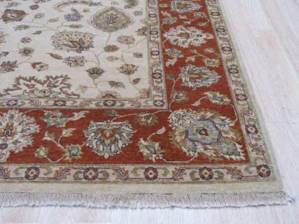 Low-pile rug with a cream field and rust floral border resting on pale wood flooring.