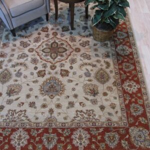 Traditional cream rug with rust border and floral medallions anchors an armchair and side table on wood flooring.