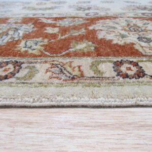 Low angle view of a cream and rust floral patterned rug edge on light wood flooring.