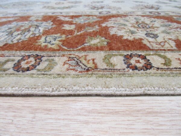 Low angle view of a cream and rust floral patterned rug edge on light wood flooring.