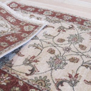 Cream low-pile rug with rust borders and muted green floral vine pattern rests on wood flooring.