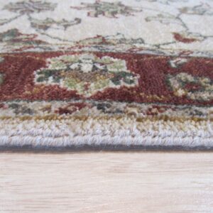Edge detail of a medium-pile cream, red, and green patterned rug on light wood flooring.