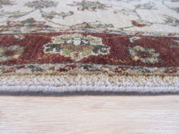 Edge detail of a medium-pile cream, red, and green patterned rug on light wood flooring.