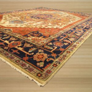 Ornate medallion rug in cream, navy, and orange, displayed on light wooden plank flooring.