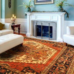 Ornate traditional rug in red, gold, and black centered between a white sofa and fireplace on a wood floor.