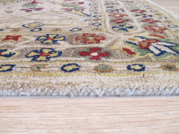 A close profile view of a beige rug featuring red, blue, and green floral details on wood floor.